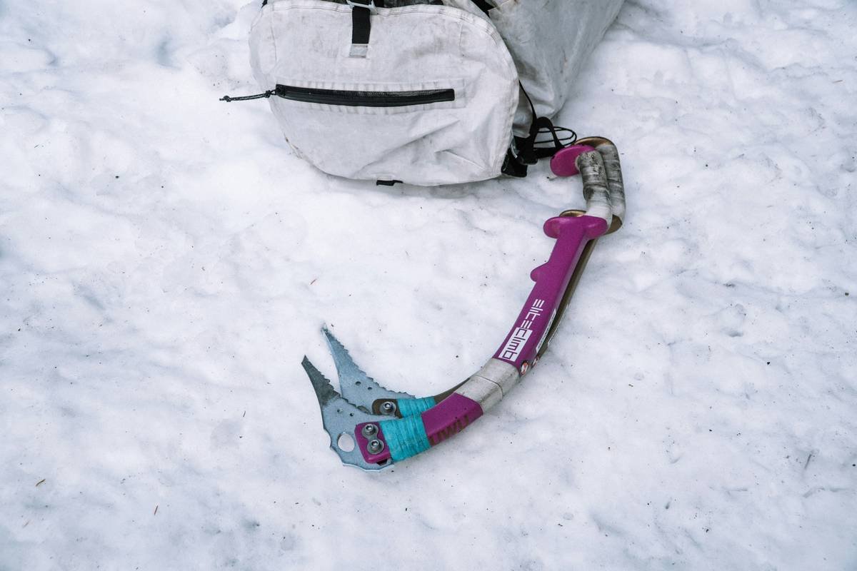 A climber hammering an ice piton into a vertical ice wall